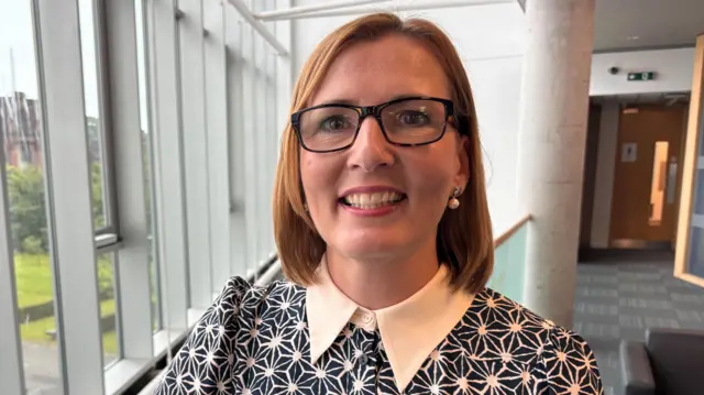 Donna Stewart wearing a blue and white patterned shirt and glasses.