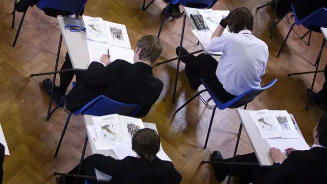 Four school pupils at desks with exam papers