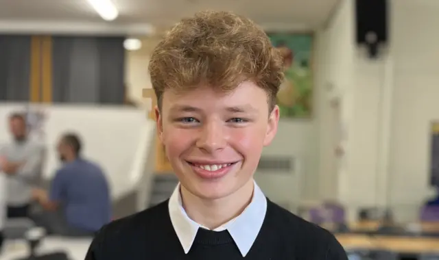 Aleksander Raczynski smiles at the camera. He has short brown hair and wears a white shite and black jumper