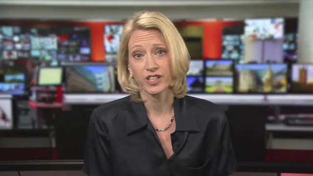 Woman with blonde hair, in a black blouse, sat in front of a TV gallery