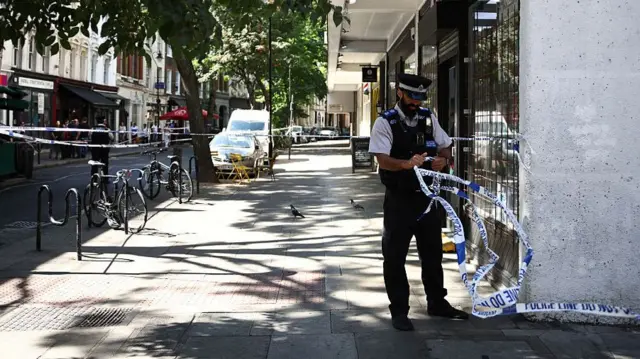 BRITAIN-CRIME A Police Community Support Officers (PCSO) removes police tape from a cordon, at Endell road in covent garden, central London on August 5, 2026. A woman was arrested after four men were stabbed in Covent Garden, a busy area of central London popular with tourists, the Metropolitan Police said on August 5