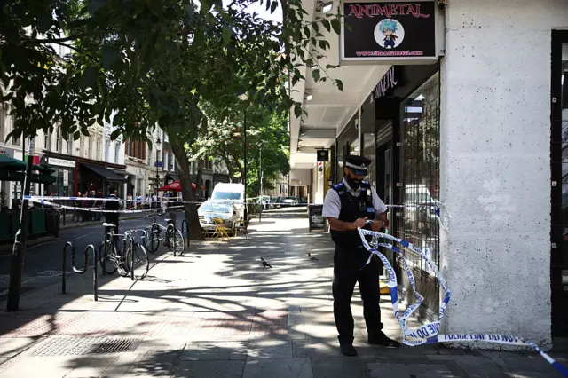 A Police Community Support Officers (PCSO) removes police tape from a cordon, at Endell road in Covent Garden,
