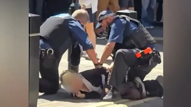 Picture of a woman being arrested by two police officers (suspect's face blurred)