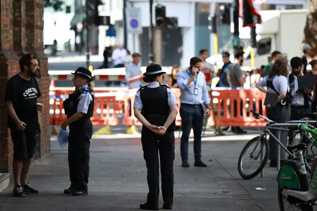 Police community support officers (PCSOs) stand behind cordon tape at Endell road in Covent Garden