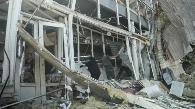 People among rubble in a building that has been destroyed, and is wonky and falling to pieces