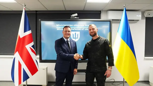 Streeting and Khmara shake hands in front of a tv screen. A British flag is next to Streeting, and a Ukrainian one next to Khmara