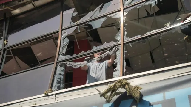 A man removing glass from smashed in windows on an upper story of a building