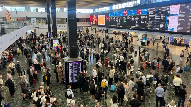 A crowd of people look up to scheduling boards at London's Euston station amid rail disruption