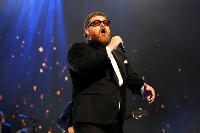 man in suit with sunglasses on, singing on a stage
