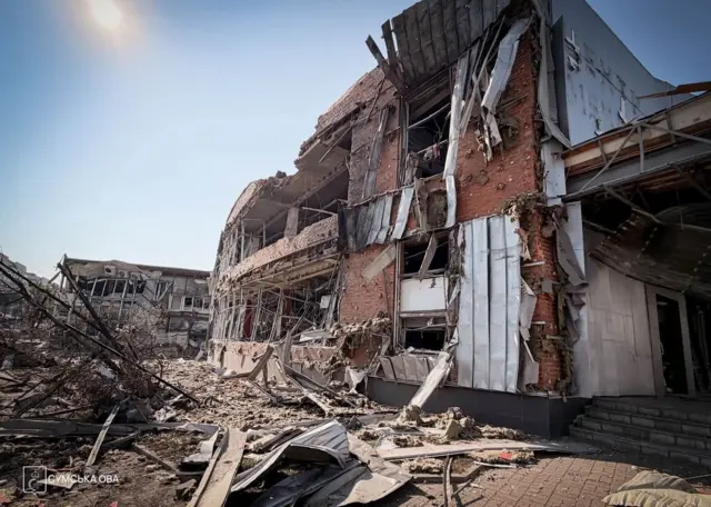 A shop front which has been destroyed, with blown out windows a damaged roof and rubbed strewn on the ground