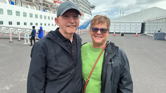 A man wearing all black and a cap and a woman wearing a black coat and green jumper
