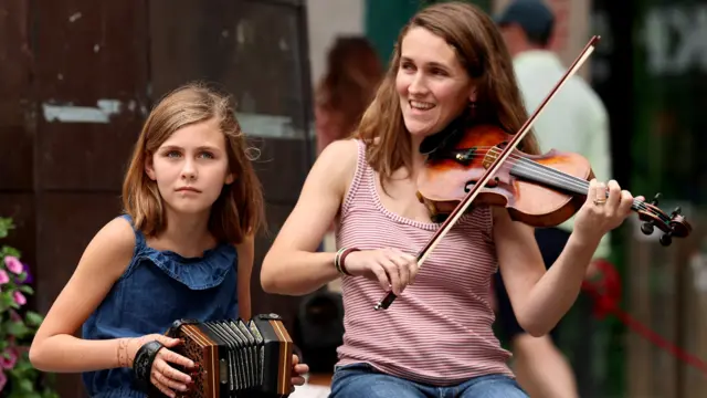 A girl with dark hair plays music beside her mum who also has dark hair