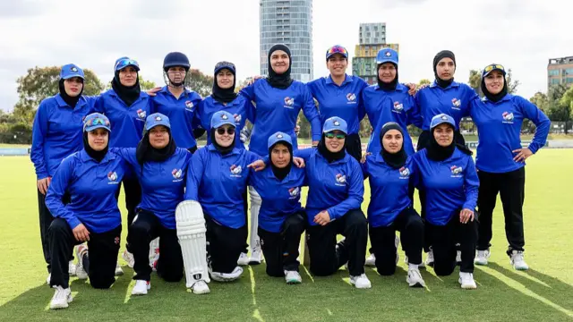 A group of women in cricket gear and headscarves are pictured on a cricket pitch.