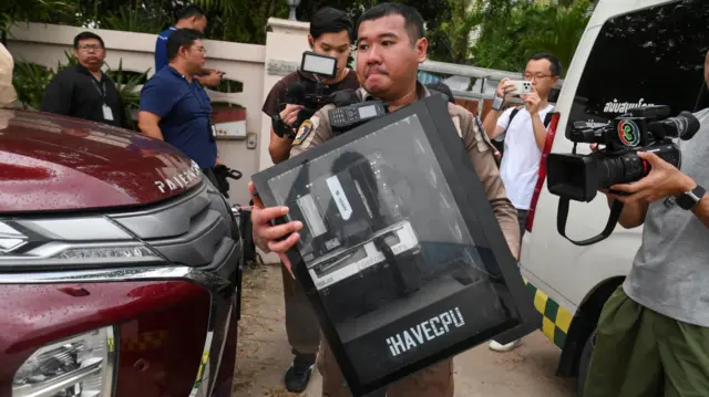A police officer carries a computer out of a residence