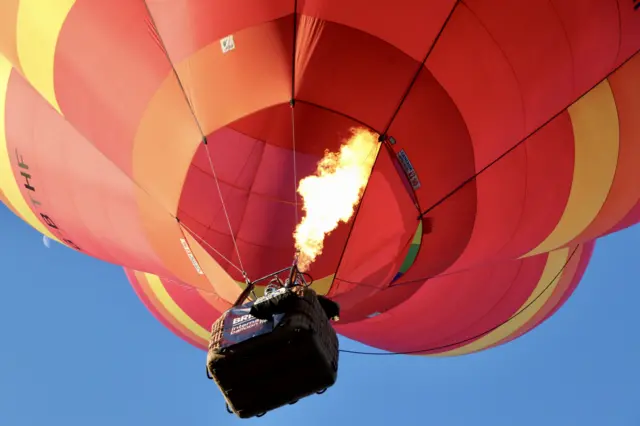 From beneath an airborne hot air balloon which is yellow, red and orange