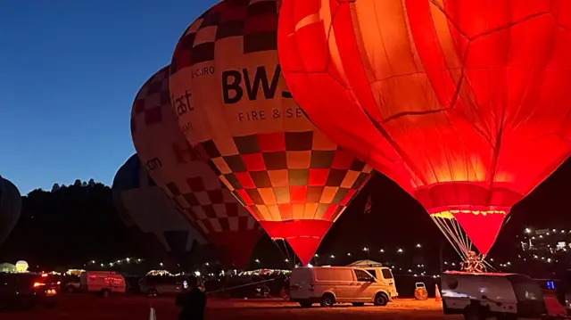 Four hot air balloons fire their burners against a dark blue sky