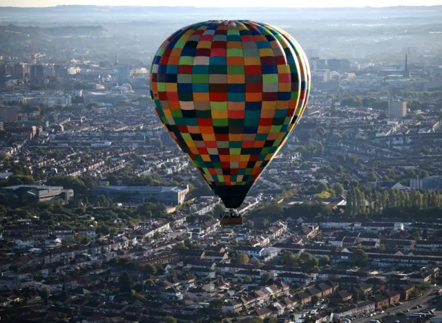 A colourful hot air balloon is seen in the air with the city of Bristol beneath it