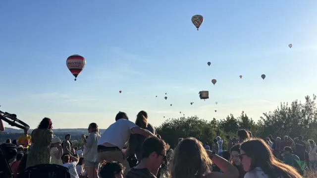 People sit on a hill with balloons in the sky