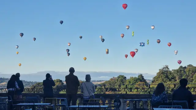 People sat on a cafe terrace looking at balloons flying in the sky