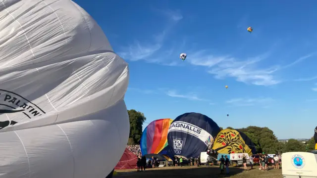 Balloons are preparing to launch with others visible in the sky in the distance