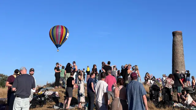 People stand on the hill with chimney and balloons