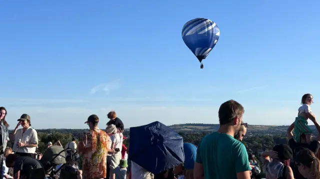 People sit on a hill with balloons in the sky
