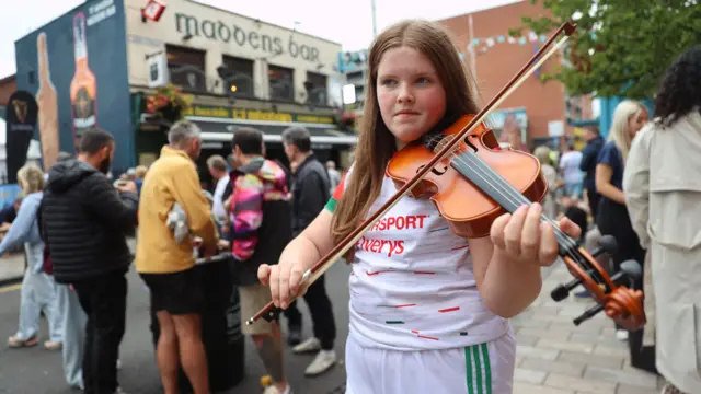 A girl wearing a white GAA top playing the violin