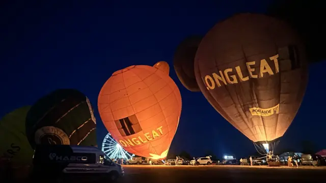 Two hot air balloons with "longleat" written on them glow as they are inflated while tethered to the ground