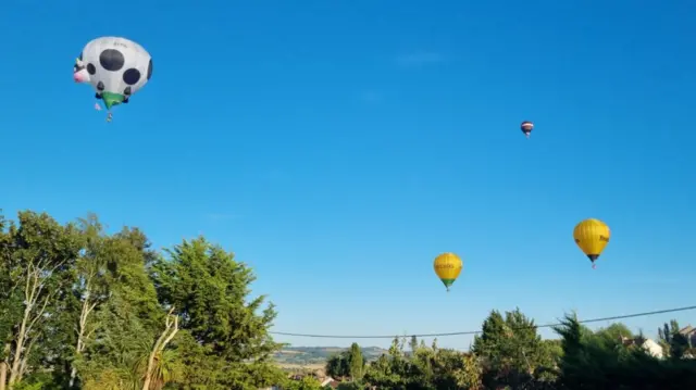 Four hot air balloons are seen in the distance against a blue evening sky