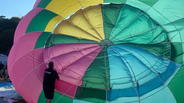 A multi-coloured balloon is being prepared by a man