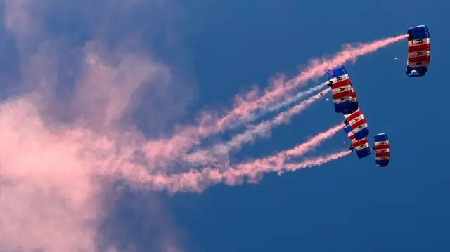 Pink smoke in the sky with blue, red and white parachutes