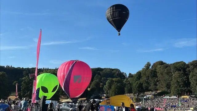 A black hot air balloon takes flight with two others still on the ground.