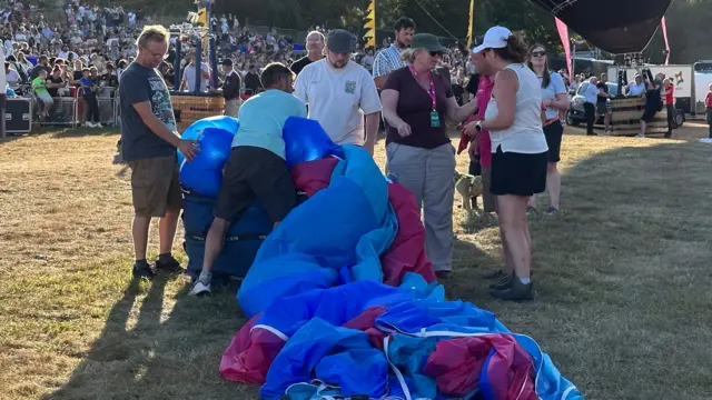 A group of balloon crews packing a pink and blue hot air balloon envelope into a bag.