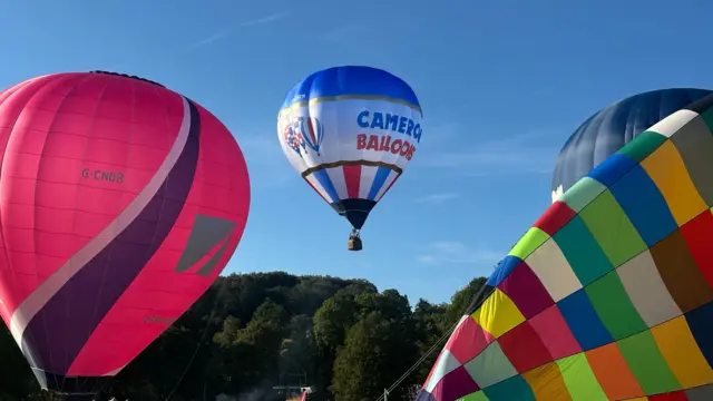 One balloon in flight behind two being prepared