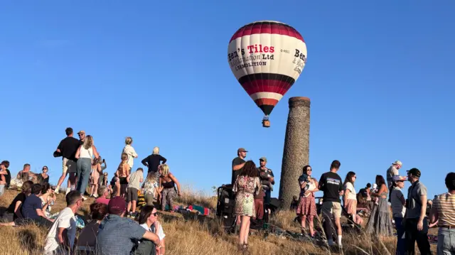 People stand on the hill with chimney and balloons