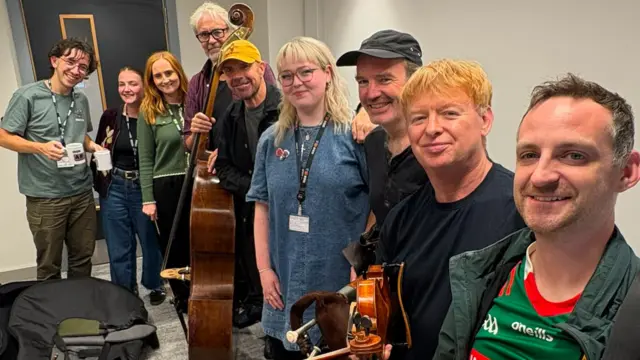 9 people pose for a picture, some are holding instruments