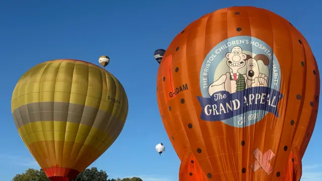 An orange Grand Appeal Aardman balloon next to a yellow balloon