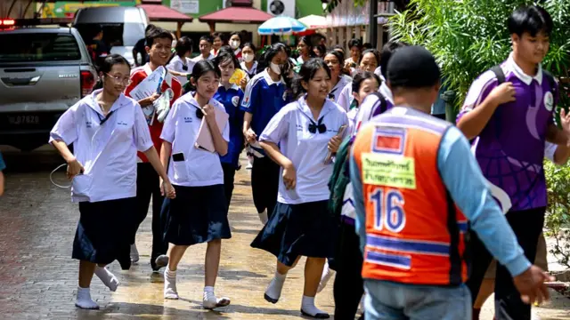 A large group of students, mostly girls, is shown running out of a school campus.