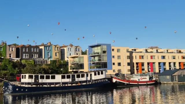 Boats and coloured houses in Bristol Harbour with balloons above in the sky.