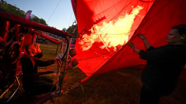 The basket of a hot air balloon is on its side as the crew fire flames from its burner inside the canopy as they inflate it