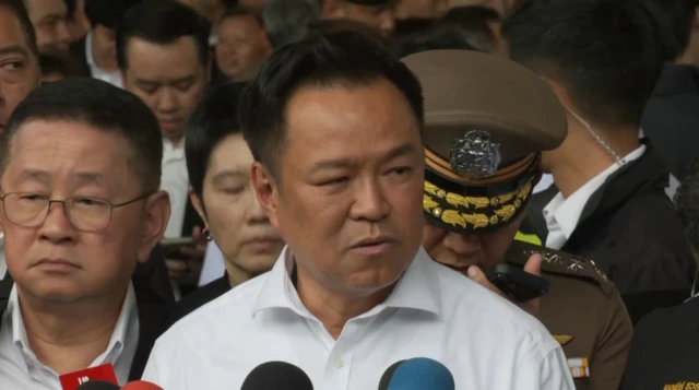 Anutin Charnvirakul in a white shirt holding a press conference surrounded by eople