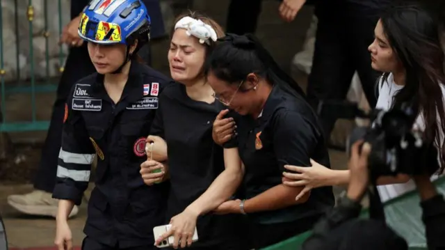 A grieving woman is supported by several others, including an emergency responder.