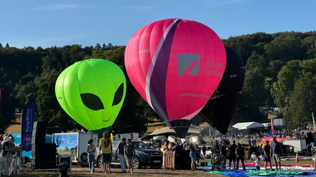 Two hot air balloons are being set up in front of a crowd