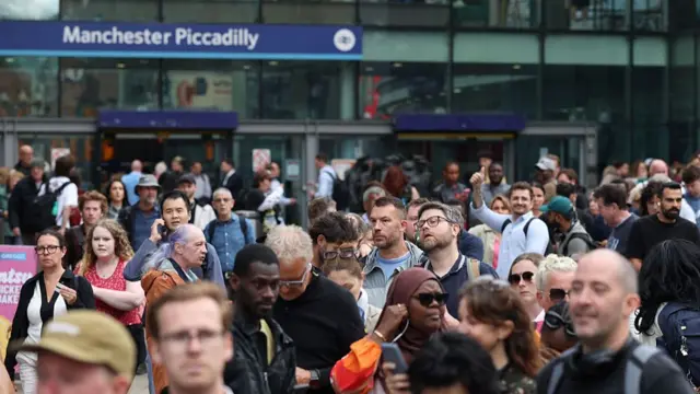 Passengers gather outside Manchester Piccadilly train station after a major disruption to rail service in the midlands and north-west England on 6 August