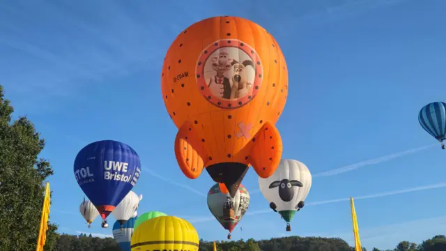 A bright orange rocket-shaped balloon with Wallace and Gromit on it hovers above the ground. In the background there are lots of other balloons, including one shaped like Shaun the Sheep.