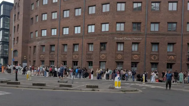 A long queue of people waiting for a bus in Bristol city centre.