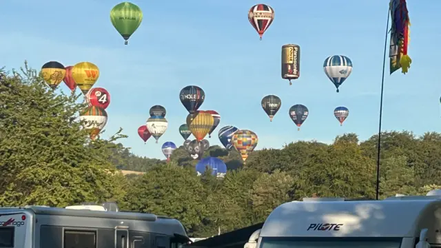 Lots of multi-coloured balloons take off, with a campsite in the foreground.