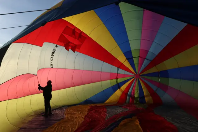 A man stands inside a colourful hot air balloon, which is half deflated on the floor, as he prepares it for flight