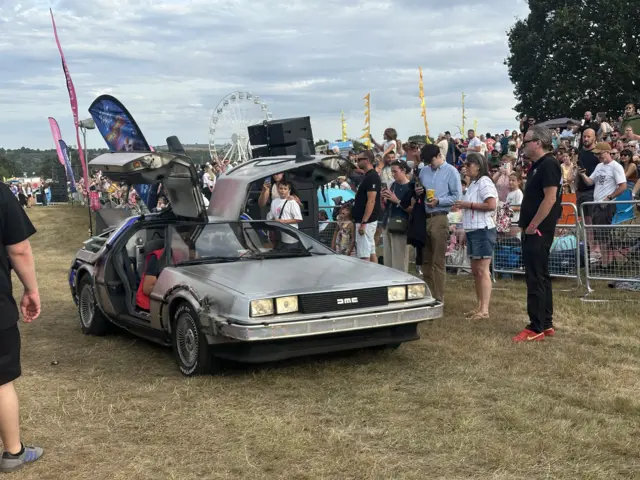 A DeLorean car with its doors up is surrounded by a crowd at Bristol Balloon Fiesta