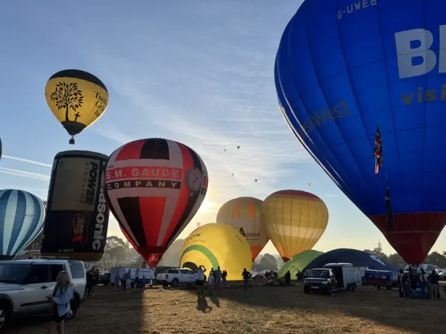A field full of balloons taking off, with the hazy sunlight peeking through.